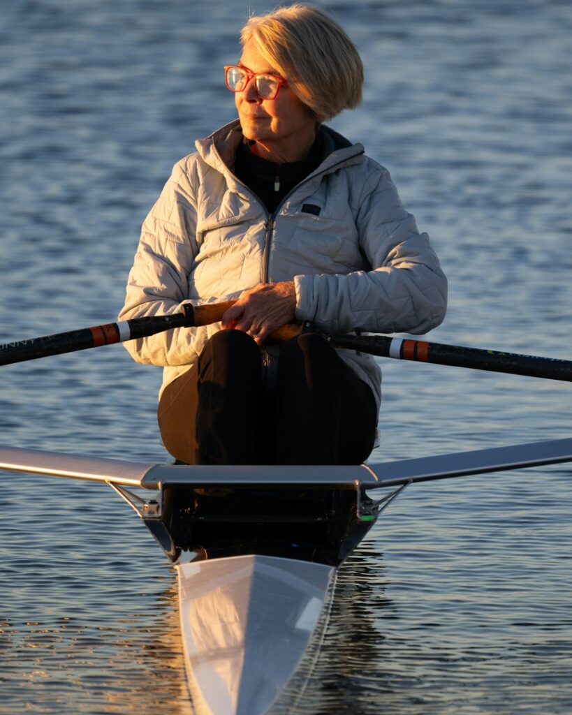 Mulher rema ao nascer do sol em bote single scull sobre água espelhada — remo em Brasília
