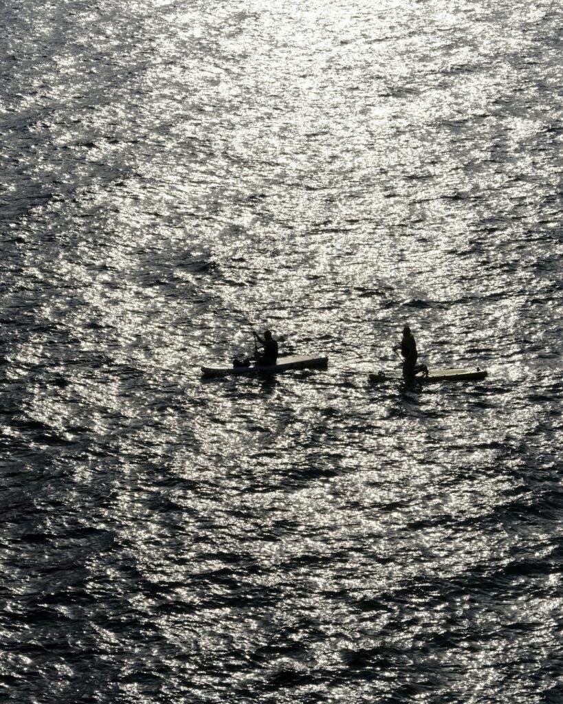 Dupla remando lado a lado em canoa havaiana sobre água escura, vista lateral