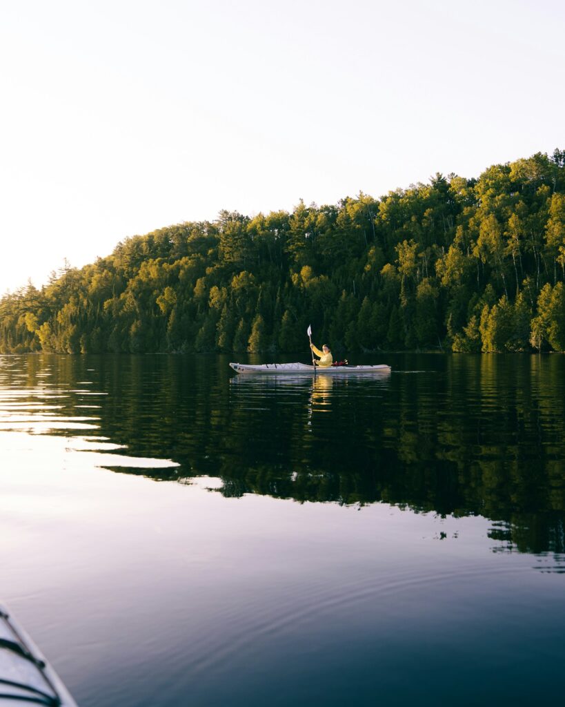Caiaque solitário desliza em lago calmo com árvores refletidas na água — cena de remo no Lago Paranoá