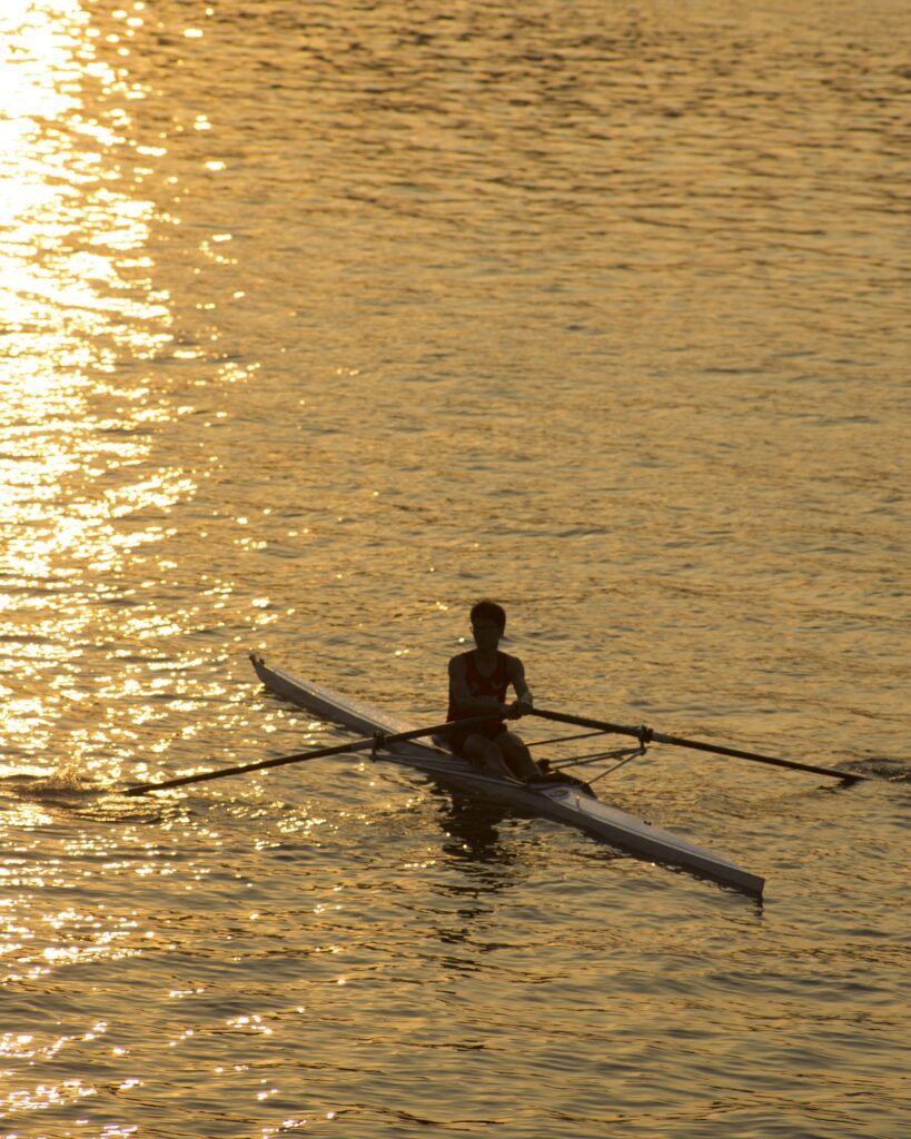 Remador solitário em contraluz dourada sobre água cintilante, silhueta ao entardecer